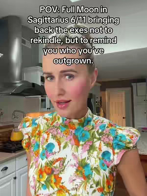 The cover image features a woman in a kitchen setting, facing the camera with an expression of focused attention. She is fair-skinned, with light-colored hair and rosy cheeks. She is wearing a colorful floral blouse with a high neckline. Behind her, a stainless steel range hood and a glimpse of a kitchen counter can be seen, creating a bright domestic backdrop.