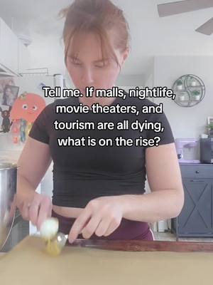 A woman with auburn hair, tied up, stands in a kitchen setting, holding a spoon and what appears to be a food item on a countertop. Text overlayed in the center asks about rising trends if malls, nightlife, movie theaters, and tourism are dying.