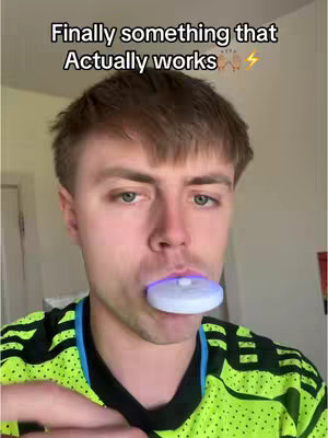 A young man with short brown hair is centered in the frame, looking directly at the camera with a focused expression. He is wearing a neon green and black soccer jersey. In his mouth is a white, circular device, likely for teeth whitening. The hook reads "Finally something that Actually works". The background is subtly blurred, with a glimpse of a plain wall and a door frame.