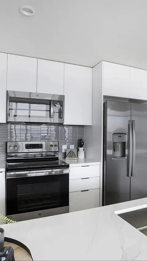 A clean, modern kitchen is shown, featuring white cabinetry, stainless steel appliances, and a light-colored countertop. The composition is a vertical shot, emphasizing the kitchen's functionality and aesthetic appeal.