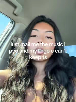 A selfie-style shot taken from inside a car. The primary focus is on a young woman with long, dark hair who is looking directly at the camera. She has a light skin tone and is wearing a light-colored top. Text is overlaid on the image, with the background showing a sky, the car's interior.
