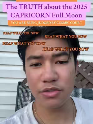 The cover image is a selfie-style shot featuring a young man centered within the frame. He's positioned against an out-of-focus outdoor background. Above his head, a series of overlaid text elements create a layered design. The top layer features text in a light purple banner that reads, "The TRUTH about the 2025 CAPRICORN Full Moon." Below that is an orange banner that states, "YOU ARE BEING JUDGED BY COSMIC COURT." Further down, the words, "REAP WHAT YOU SOW," are repeated multiple times in stacked and slightly offset lines around the man's head, written in a distressed, orange font. The man, with short black hair, is wearing a white shirt and a gold chain necklace and looks directly at the viewer with a neutral expression. Behind him, out of focus, is a wooden fence.