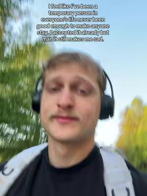 A man with headphones is the focus, set against a blurred outdoor backdrop with greenery. Text overlays the image, conveying a somber reflection.