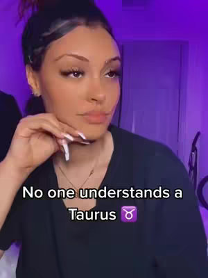 A woman, with dark hair styled in a side bun, gazes thoughtfully off-camera. She's wearing a dark top and a delicate necklace. The background is softly lit in purple.