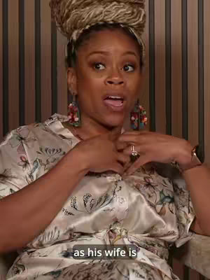 A woman with a head wrap and large earrings speaks while gesturing with her hands. A text overlay at the bottom reads, 'as his wife is'.