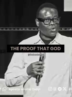 A grayscale image of a man speaking into a microphone. He is wearing glasses and a light-colored shirt. A black rectangular text overlay at the center of the image reads, in white, "THE PROOF THAT GOD". The background is blurred.