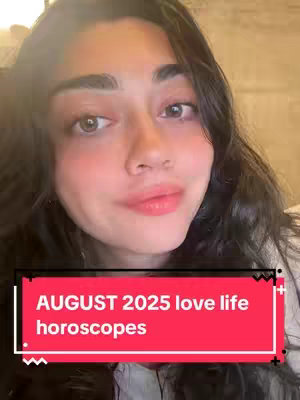 A selfie-style image featuring a light-skinned woman with dark hair, gazing towards the camera. She has full lips, light eyeshadow, and appears to be making a subtle smile. A red banner in front of her face contains text. The background is softly blurred, which emphasizes the woman.