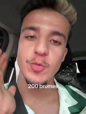 A young man with a mustache, has light skin and dark eyes, is seated in a car with a white and green patterned shirt, with text '200 brumes' overlayed on the image.