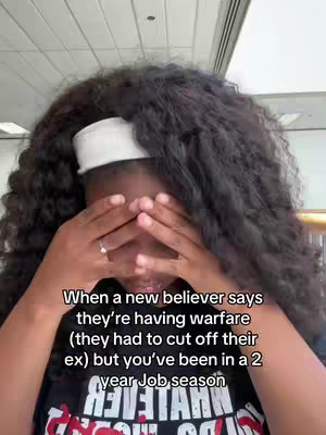 A selfie image shows a dark-skinned person covering their face with their hands, with visible tears. The text overlay reads, 'When a new believer says they're having warfare (they had to cut off their ex) but you've been in a 2 year Job season.' The person wears a white headband and a black t-shirt with a design. The background is a blurred interior space, possibly an airport or a similar public area.