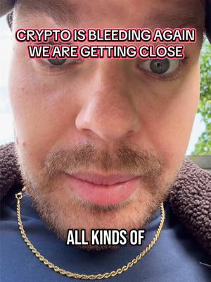 A close-up shot of a man's face, with visible text overlay. He has short, dark hair, a beard, and is wearing a gold chain. The background is slightly blurred, with a suggestion of greenery.