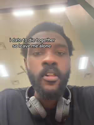 A close-up shot of a man's face. The man has a dark beard and is wearing headphones around his neck. Text overlayed on the image reads "i date to die together so leave me alone".