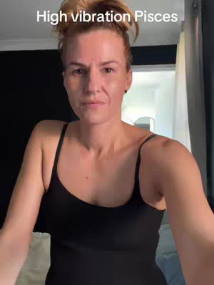 A woman with light skin and red hair. The woman is looking at the camera. She is wearing a black tank top. The image is well-lit.