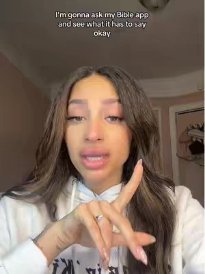 A woman with long brown hair is in a close-up shot. She wears a white hoodie and is pointing with her right index finger. Text is added to the top of the screen.