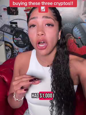 A woman with long dark hair, wearing a white top, is the focus of a selfie. The text overlay states, 'buying these three cryptos!!'. She is in the middle of speaking, with her mouth open.
