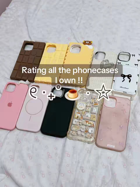 A top-down shot displays various phone cases arranged on a white, textured surface, possibly a bedspread. The cases are diverse in design. In the center, a text overlay reads, "Rating all the phonecases I own !!". Icons and emojis are scattered around the cases.
