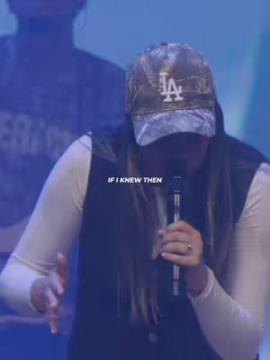 The cover image showcases a person, wearing a camo LA Dodgers hat, a black vest over a long-sleeved white T-shirt, positioned in a medium shot. A microphone is held in their right hand and their mouth is close to it as if they are singing . The image, bathed in a blue hue, also displays text overlayed at the middle of the image.