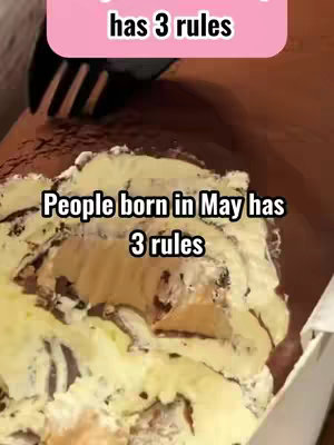 The image shows a close-up of what seems to be a piece of cake with white frosting and dark chocolate shavings, positioned in a cardboard box.