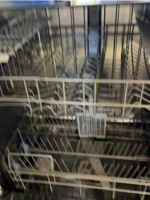 An interior shot of a dishwasher. The image is a slightly blurry view inside the dishwasher, with vertical metal racks and supports visible. The lighting is a bit dim, suggesting the inside of the appliance.