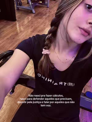 The cover image is a selfie-style shot featuring a young woman with long, light brown hair in a braid, a pink scrunchie, and a black top. She's positioned slightly off-center, angled towards the camera. The background appears to be a gym or exercise room, suggested by the blurry equipment and the slightly warm lighting. Text overlayed at the bottom gives a quote about wanting to use her career to help those with no voice.