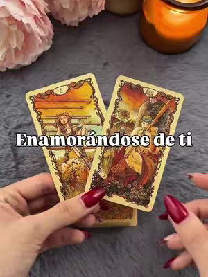 The cover image depicts a hand holding two tarot cards in front of a blurred background with candles and a floral arrangement. The woman's hand has long red nails. The text overlayed on the cards reads: "Enamorándose de ti."
