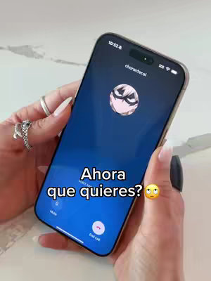 A person's hands hold a smartphone with the screen displaying a call from "characterfcai". The phone screen has text overlayed that says "Ahora que quieres?" with a worried emoji.