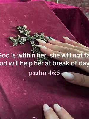The image shows a close-up of a hand with long, manicured nails, resting on a dark red, velvety surface. A detailed, ornate silver cross is lying on the fabric. Text is overlaid on the image, conveying a religious message.