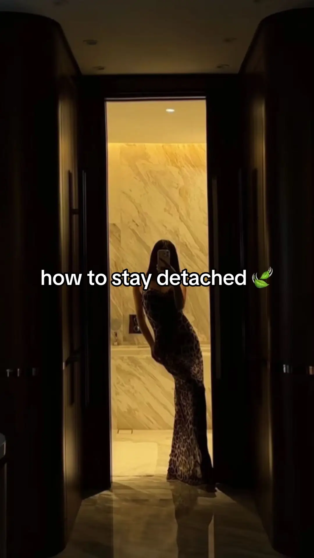 A woman in a dark room is standing in front of a mirror, in a leopard-print dress, taking a photo of herself. The text overlaid reads "how to stay detached".
