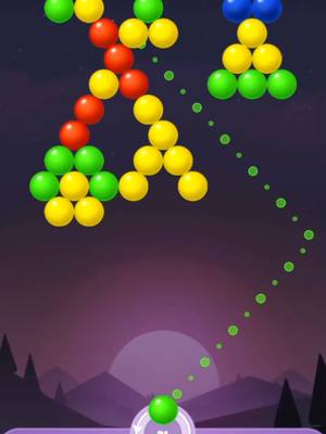 A screen capture from a mobile bubble shooter game. Various colored bubbles are arranged in clusters, with a trajectory line indicating a shot being taken. The background shows a purple sky with a stylized sun setting over silhouettes of trees.