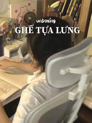 The cover image shows a person from behind, sitting in a chair and working at a desk. The chair is the focal point. In the background, partially visible, are shelves with books and other items. On the desk, a notebook is open to a page of text. The background is a bit cluttered with various items, creating a cozy, lived-in atmosphere. The color palette is soft and natural.
