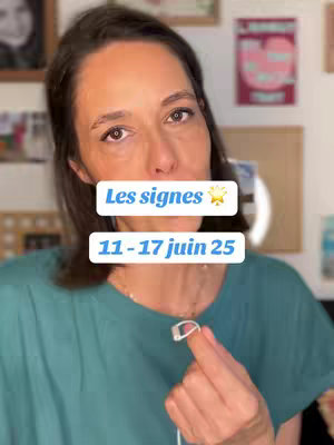 A woman with brown hair is centered, facing the camera. She wears a teal top and holds a microphone.  Text overlays in white boxes read "Les signes" with a star and "11-17 juin 25." Background is blurred, including art and framed pictures.