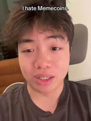A selfie-style video cover image features a young person framed from the chest up, centered against a neutral background. The subject, presumed to be the content creator, has dark hair and is wearing a gray shirt. The person looks directly into the camera, with a text overlay at the top stating, "I hate Memecoins."