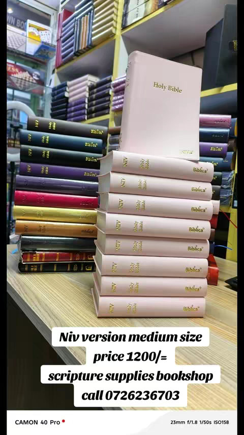 A vertical shot showcasing rows of Bibles, books, and shelves filled with various books. The foreground is dominated by a stack a pink Bibles. Additional text is overlaid on the image, offering pricing details and contact information for scripture supplies.