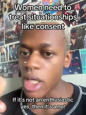 A young person with short, light-colored hair is centered in the frame, looking directly at the camera with an open mouth. They have a nose piercing and are wearing a black top. Above them, text is displayed, and the background is covered with various posters and pictures.
