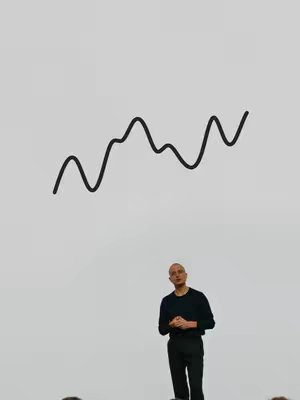 A minimalistic image featuring a presenter in a dark outfit against a white background. Above the presenter, a stylized black line graph representing a stock chart or financial trend is present. The presenter, a bald man, stands in a focused pose. The composition is clean and simple.