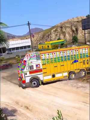 An eye-level shot captures a vibrant yellow Indian truck, prominently positioned on a dirt road. The truck is adorned with colorful decorations, typical of Indian truck art. The background shows a partially obscured building, a road, and a mountain range, suggesting a rural or semi-urban setting. The sky is blue, indicating daylight. The overall composition emphasizes the truck, with the background adding context to its environment.