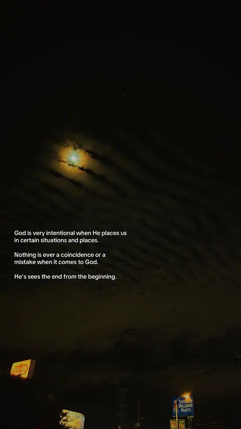 The image presents a nighttime scene with a dark, cloudy sky. The moon, partially obscured by clouds, creates a soft, yellow glow. The foreground includes the tops of buildings and illuminated signs. Text is overlaid on the image, offering a spiritual message.