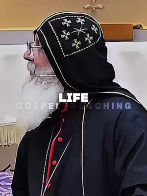 The image shows a man in religious attire, likely a bishop or other clergy member, viewed in profile. He is wearing a black robe with a red lining and a black hood adorned with gold embroidery. The background appears to be a light-colored interior, possibly a church or religious building. Text overlays are added to the image with the words "LIFE" and "GOSPEL REACIHING".