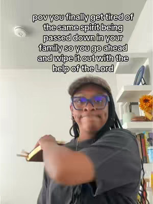 A woman with locs wearing a hat and glasses is holding a Bible and smirking. The background is a white wall with a shelf and decor. Text overlay is in white.