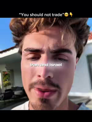 A selfie-style shot emphasizes a man's face, with a soft focus on his expression. His light brown hair is styled slightly tousled. He has a mustache and slight stubble. The background shows a hinted blue sky and architectural elements giving an impression of an outdoor setting where the sun is lighting his face.