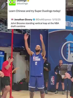 The image shows a basketball player performing a vertical leap at what appears to be a combine event. The player, wearing a blue jersey with the number 12, is mid-air with arms fully extended. In the background, there are spectators and event staff, and a Duolingo post.
