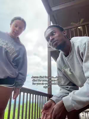A medium shot features two individuals on an outdoor porch. A woman is on the left, and a man is on the right. The woman is wearing a grey sweatshirt and looks towards the camera. The man is wearing a grey sweatshirt and looking up slightly towards the sky. Text is overlaid at the bottom, and the image is framed against a backdrop of greenery and a cloudy sky.