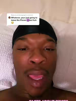 A close-up shot featuring a Black man lying down with his tongue out, seemingly in a playful or silly expression. He has a black durag on. At the top, a comment from another user is visible in a small white box. The background is blurred, likely a pillow or bedding.