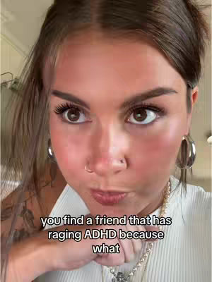 A close-up shot of a woman's face, with a direct, slightly questioning gaze. She has light skin, dark hair pulled back, and a nose piercing. The image has text overlaid at the bottom that reads 'you find a friend that has raging ADHD because what'. She is wearing a white top and a necklace.