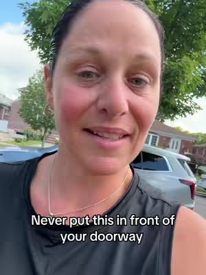 A woman is standing outside with a car and trees in the background. Text overlay reads: Never put this in front of your doorway.