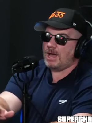 A man with a shaved head wearing sunglasses, a black baseball cap with the number '633' in orange, and headphones is speaking into a black microphone. A 'SUPERCHA' logo is in the bottom right corner.