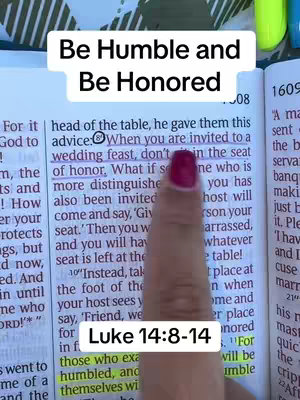 A close-up shot of an open Bible, with a finger pointing to a highlighted passage about humility and honor. A white rectangle with the text "Be Humble and Be Honored" in a bold, sans-serif font is positioned at the top of the image. Below the text, the words "Luke 14:8-14" are displayed in a white rectangle.