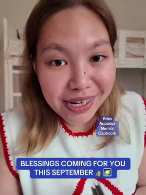 A selfie-style shot features a woman with light brown hair and fair skin against a home interior background. She is smiling and speaking directly at the camera. A bright blue rectangle with white font reading "BLESSINGS COMING FOR YOU THIS SEPTEMBER" is positioned near the bottom left. At the top right, a smaller light rectangular background displays the zodiac signs Aries, Aquarius, Gemini, and Capricorn.