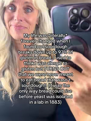 The image is a selfie-style video cover featuring a blonde woman. She is looking directly at the camera and holding a smartphone in her right hand. Text is overlaid on the image, starting with a statement about how sourdough changed her life. The background is blurry, suggesting an indoor setting.