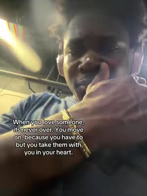 A selfie-style shot focusing on an individual's face, who appears to be holding their hand up near their face, and the text overlayed reads: 'When you love someone, its never over. You move on, because you have to but you take them with you in your heart.' The overall lighting appears dim.