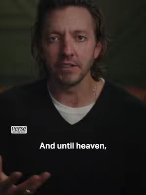 A man with dark hair and a beard is centered in the frame, gazing directly at the viewer with a focused expression. He's wearing a black V-neck shirt with a small silver cross necklace visible. The background is indistinct, with soft, muted tones. The text overlay indicates the video's content and call-to-action.